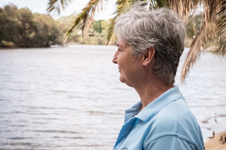 A woman with short grey hair and a pale-blue shirt looks out over a body of water.