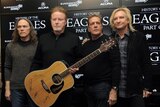 The Eagles band members standing shoulder to shoulder wearing dark-coloured knits with one man holding acoustic guirar 