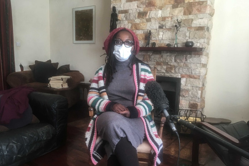 Zimbabwean novelist Tsitsi Dangarembga sits in her living room wearing a face mask and a beanie.