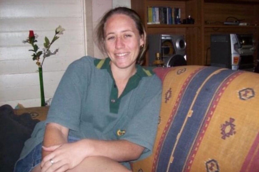 A smiling woman in a grey polo shirt sits on a couch 