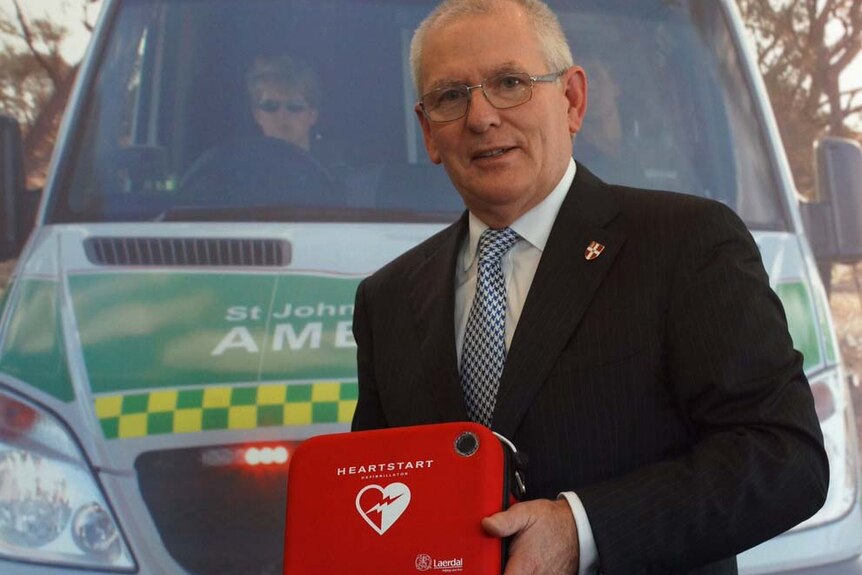 Tony Ahern holding a defibrillator in front  of an ambulance