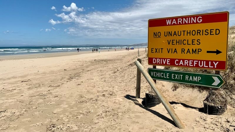 Signs directing cars to an exit ramp with a beach in the background