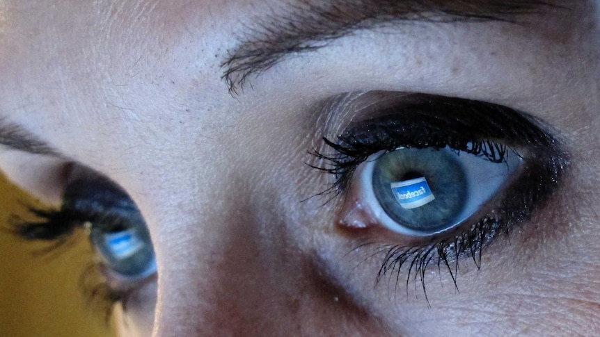 A woman looks at the Facebook website with the icon reflected in her eyes.