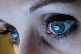 A woman looks at the Facebook website with the icon reflected in her eyes.