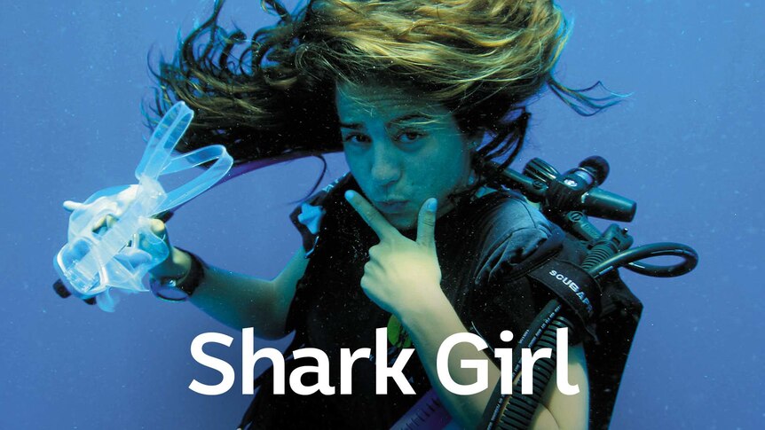 Girl posing underwater with her left hand framing her chin with her index and thumb and the other hand is holding her goggles