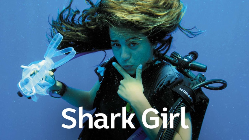 Girl posing underwater with her left hand framing her chin with her index and thumb and the other hand is holding her goggles