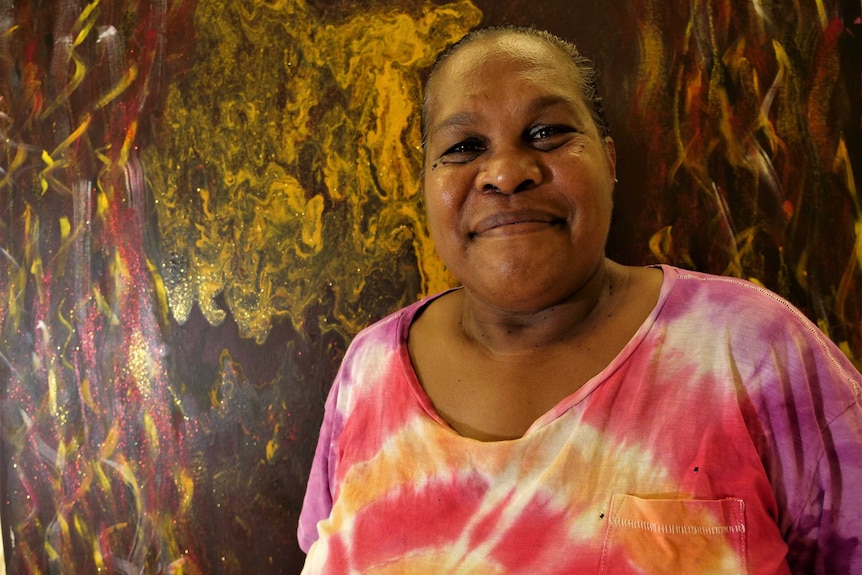 Close up of smiling woman wearing a tie-dye shirt in front of an Aboriginal painting