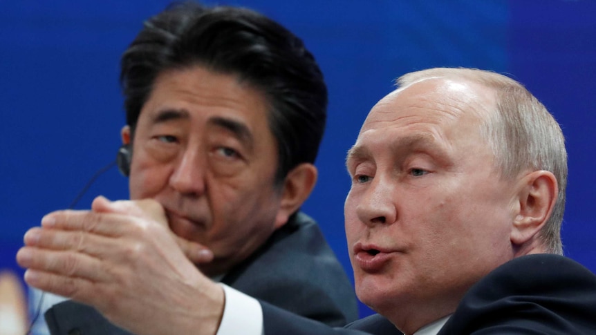 Shinzo Abe looks unimpressed as he listens to Putin talk at a forum.