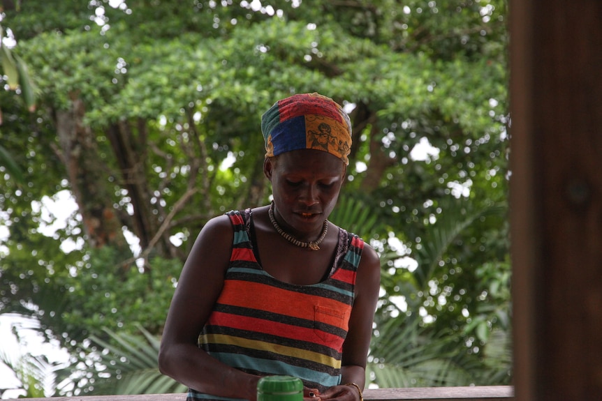 Imelda looking down, wearing an orange, black and light blue striped bandana and matching singlet. 