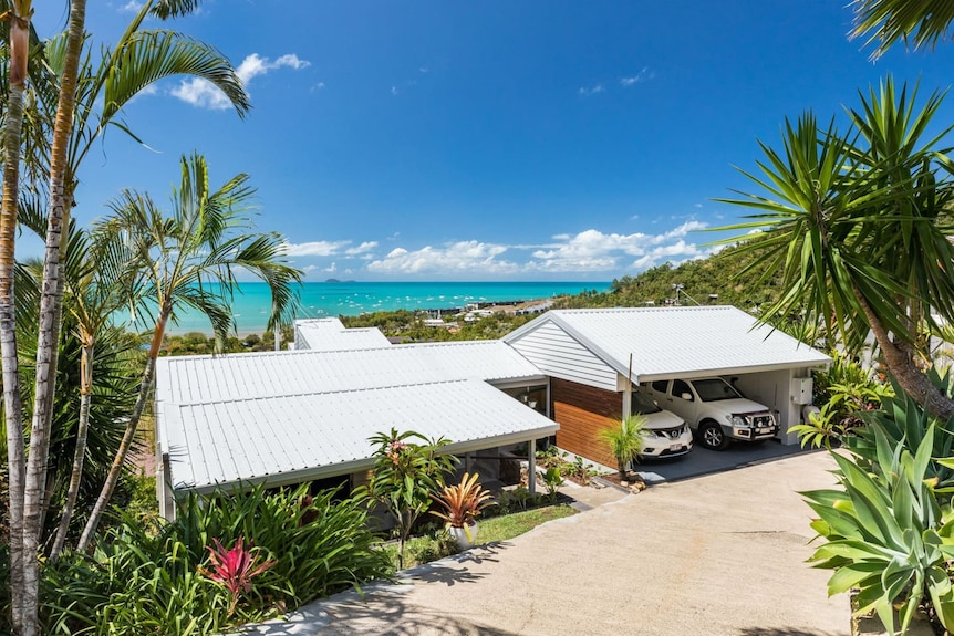 the front of a house and carport, with the ocean seen behind it