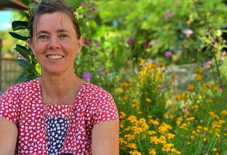 Woman sitting in flower garden smiling, pictured in story about living without money