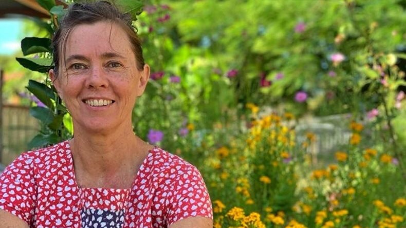Woman sitting in flower garden smiling, pictured in story about living without money