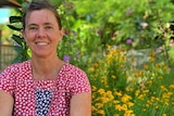 Woman sitting in flower garden smiling, pictured in story about living without money