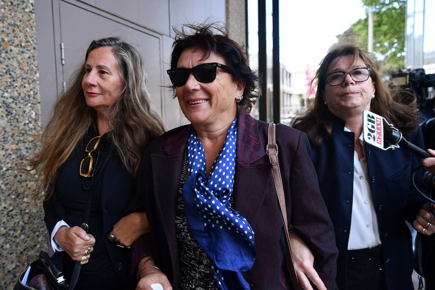 three women moving through a crowd of media