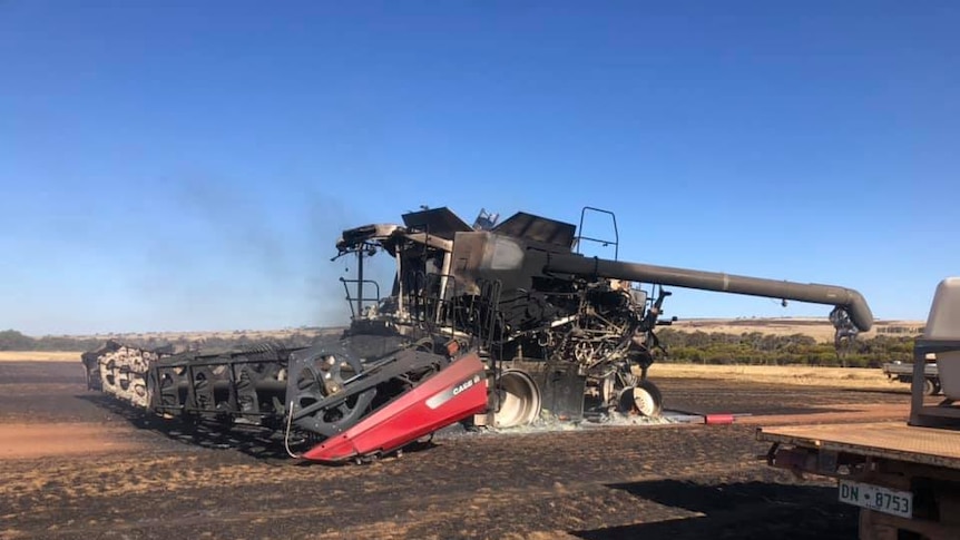 A burnt out red harvester stands in scorched farmland