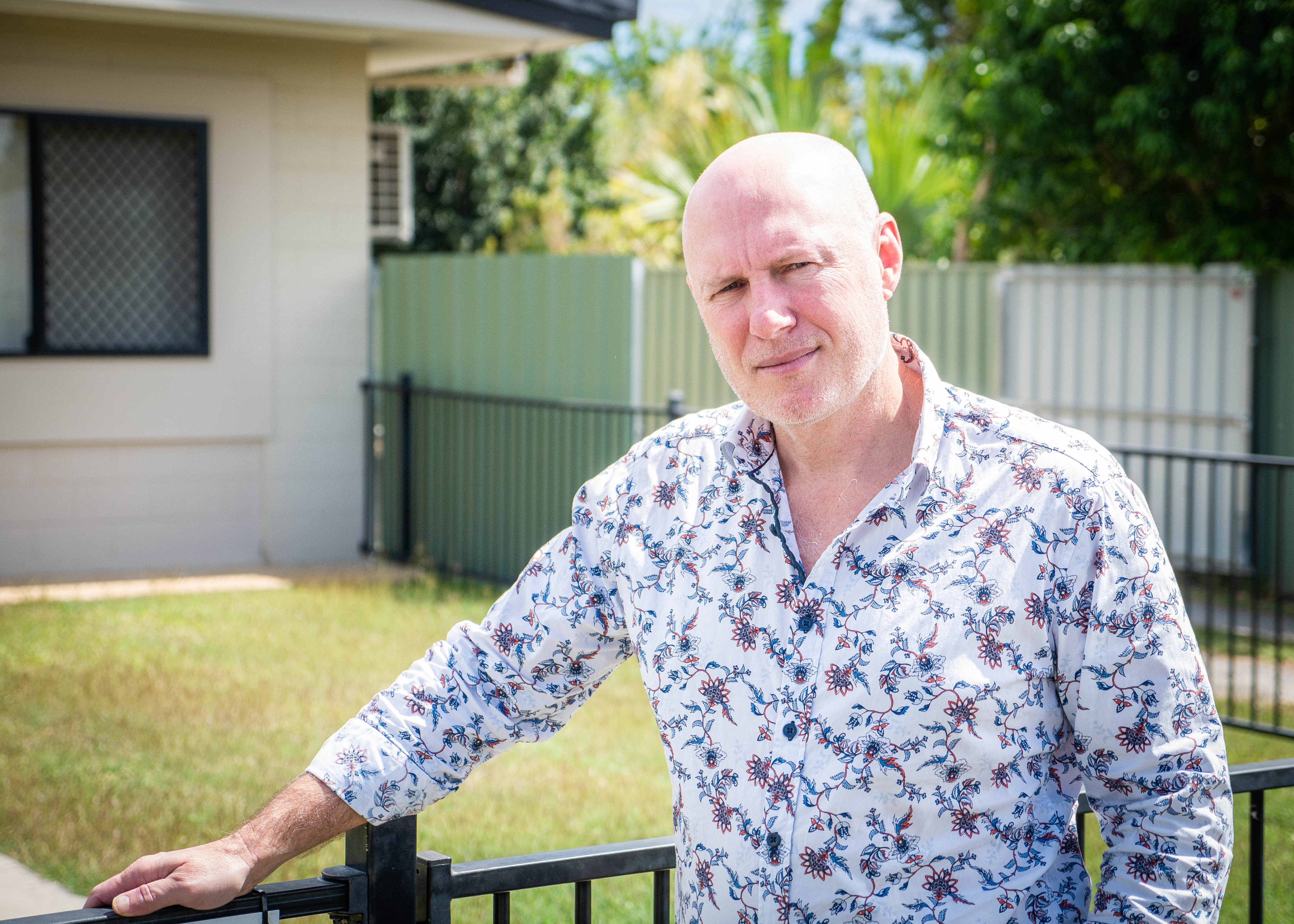 A man wearing a patterned shirt stands in front of a yard