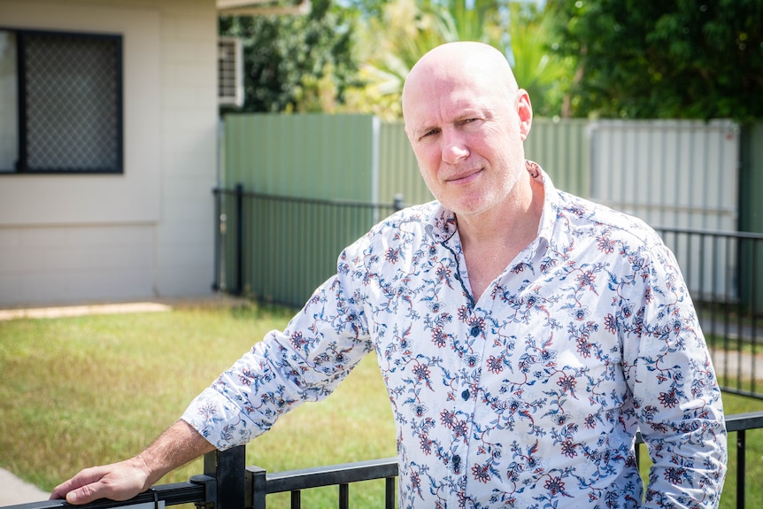 A man wearing a patterned shirt stands in front of a yard