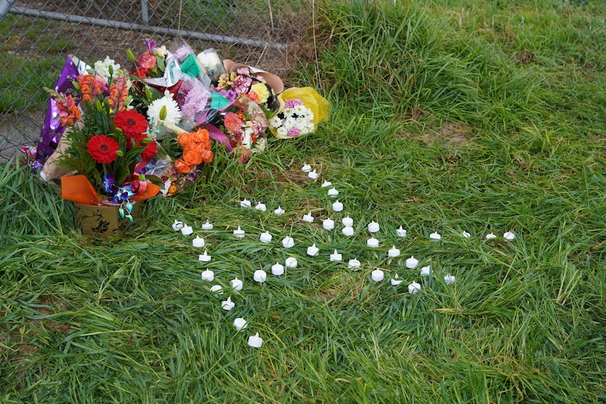 Flowers and white candles spelling the letters AK left on the grass