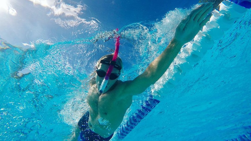 A man swimming in a pool with a snorkel mid stroke, with a blue and white lane divider next to him.