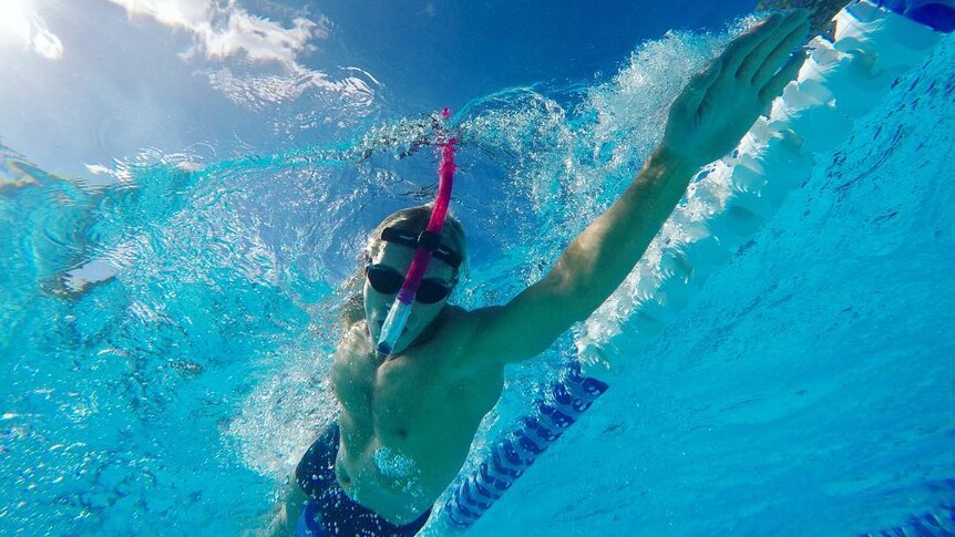 A man swimming in a pool with a snorkel mid stroke, with a blue and white lane divider next to him.