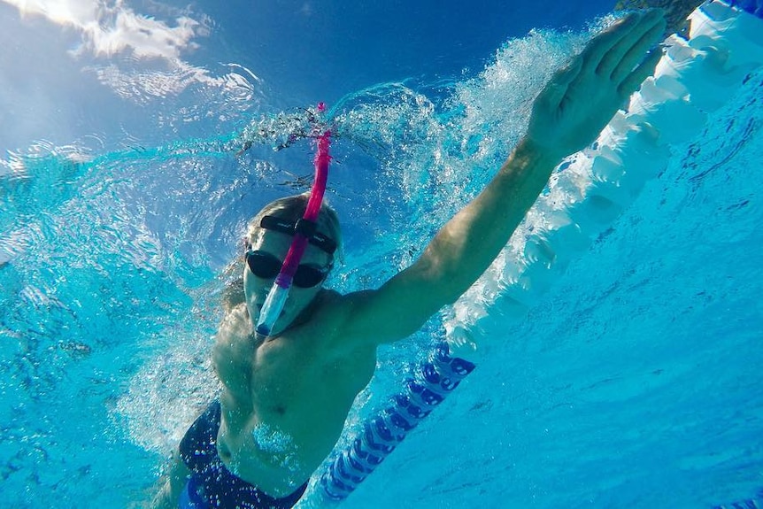 a man swimming in a pool with a snorkel mid stroke