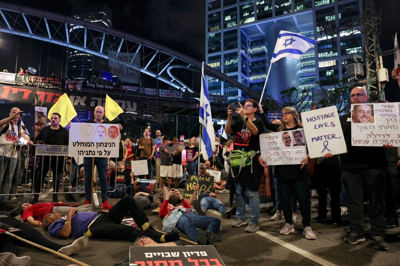 A large number of people holding signs, with several other people lying on the ground
