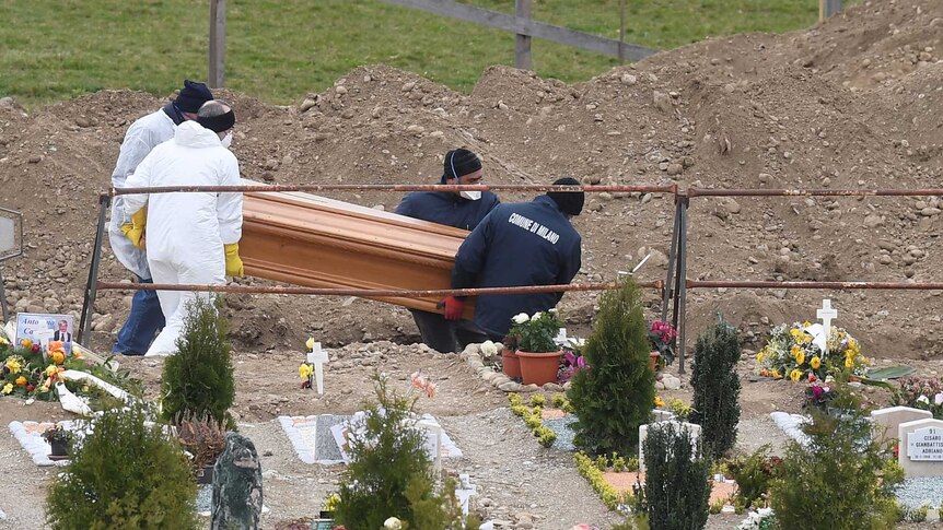 Workers place a coffin in the ground at a cemetery