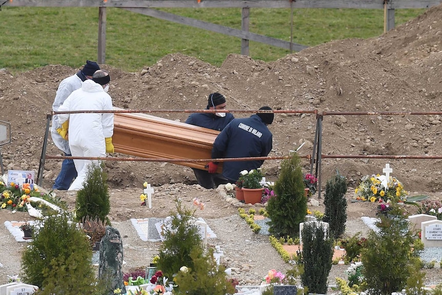 Workers place a coffin in the ground at a cemetery
