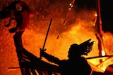 A man dressed as a viking is silhouetted against a burning Viking long ship