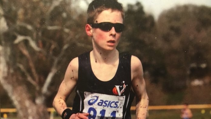 A young boy runs a race wearing sunglasses, with mud splashed up his legs.