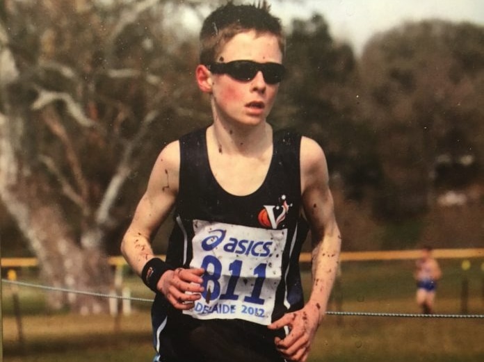 A young boy runs a race wearing sunglasses, with mud splashed up his legs.