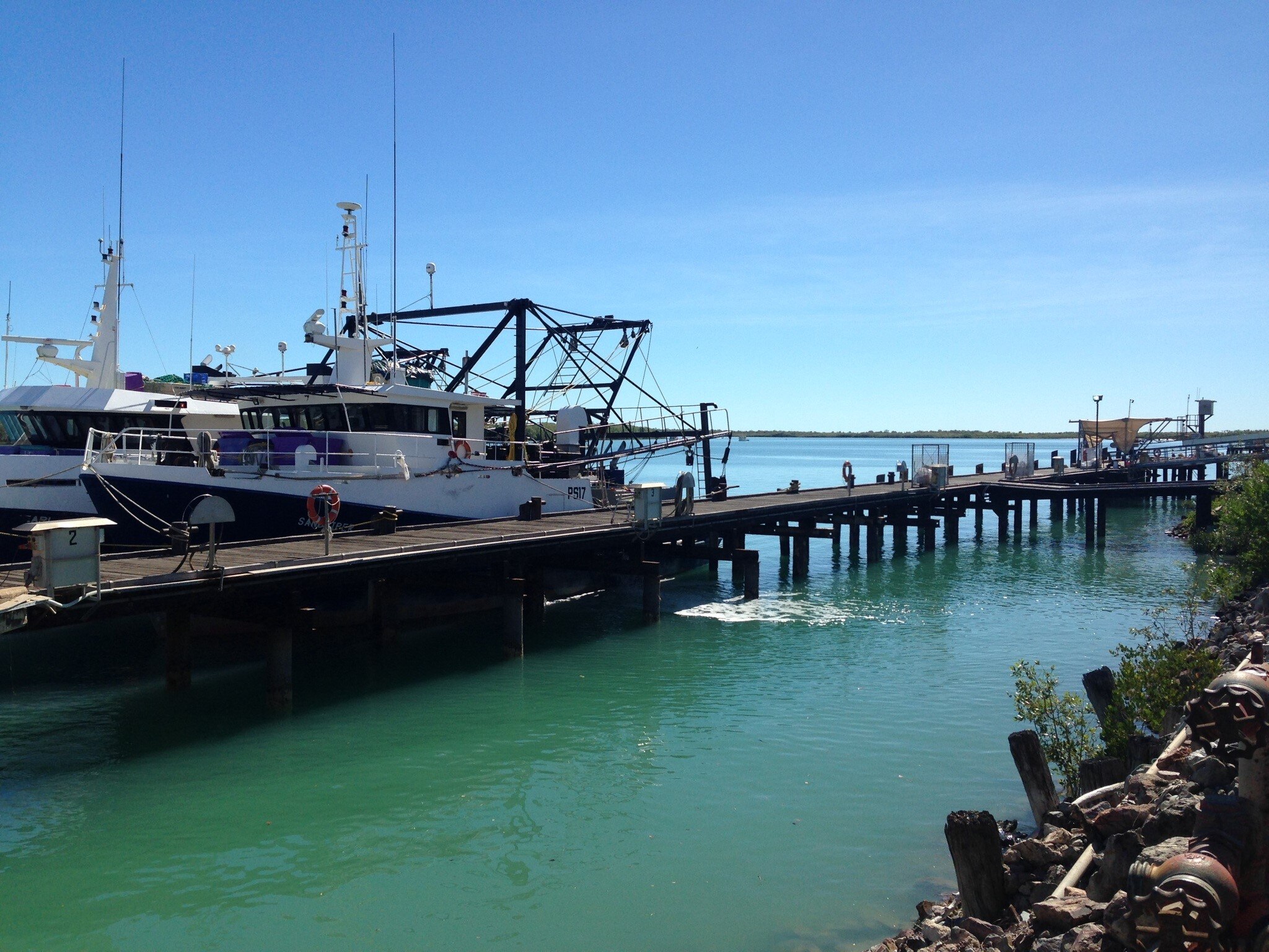 Fishing trawler boat docked next to a long pier off the coast line on a bright sunny day. 