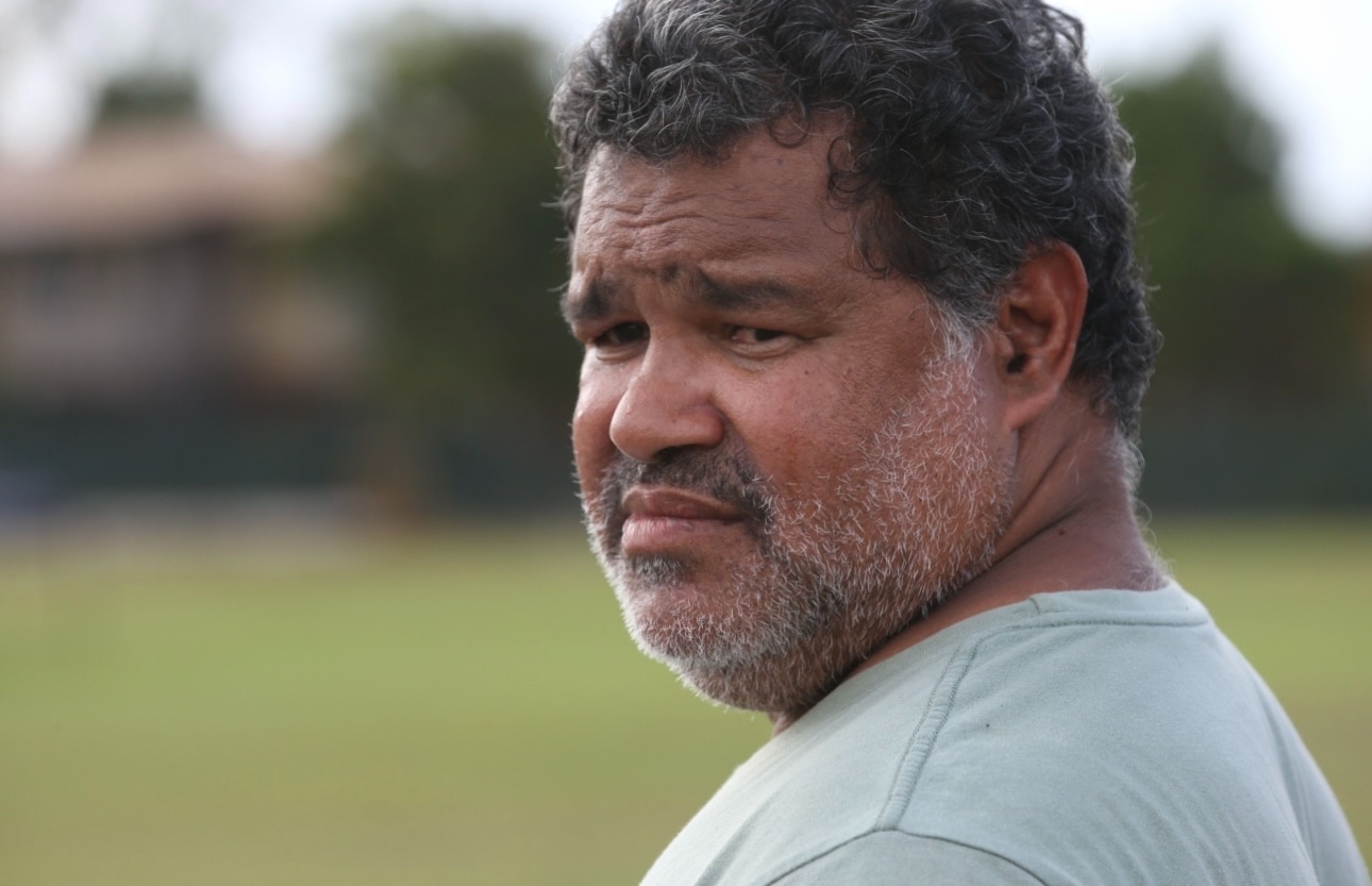 Un hombre vestido con una camisa verde claro mira hacia un lado con expresión seria.
