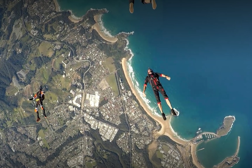 A group of men freefall from a plane while skydiving, showing the coastline below them.