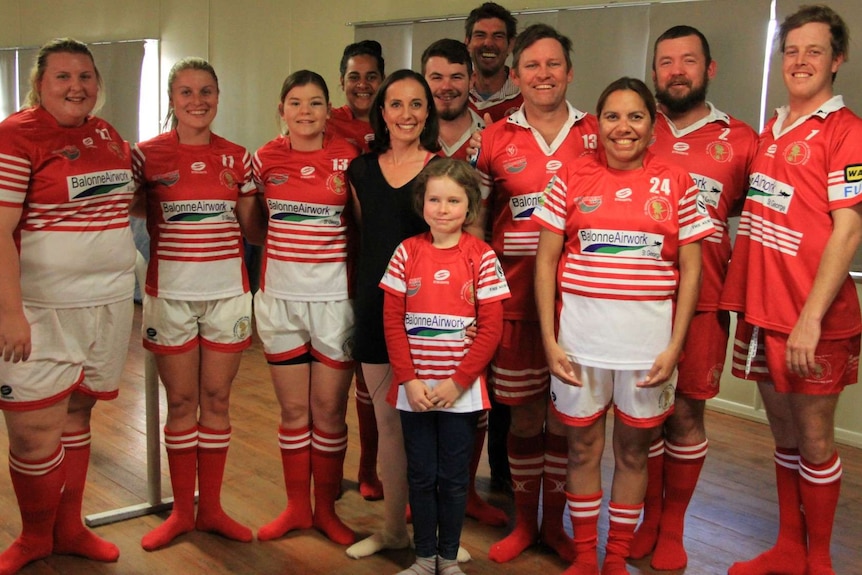 Men and women in football uniforms standing with ballet teacher Fiona Gaske after class.