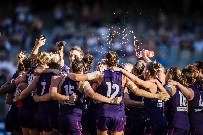 Fremantle's AFLW team celebrates in a group on the field at Perth Stadium.