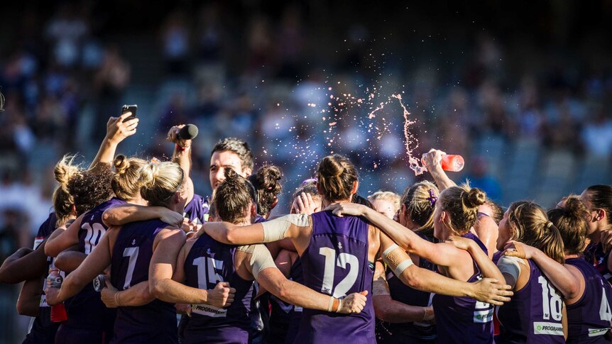 Fremantle's AFLW team celebrates in a group on the field at Perth Stadium.