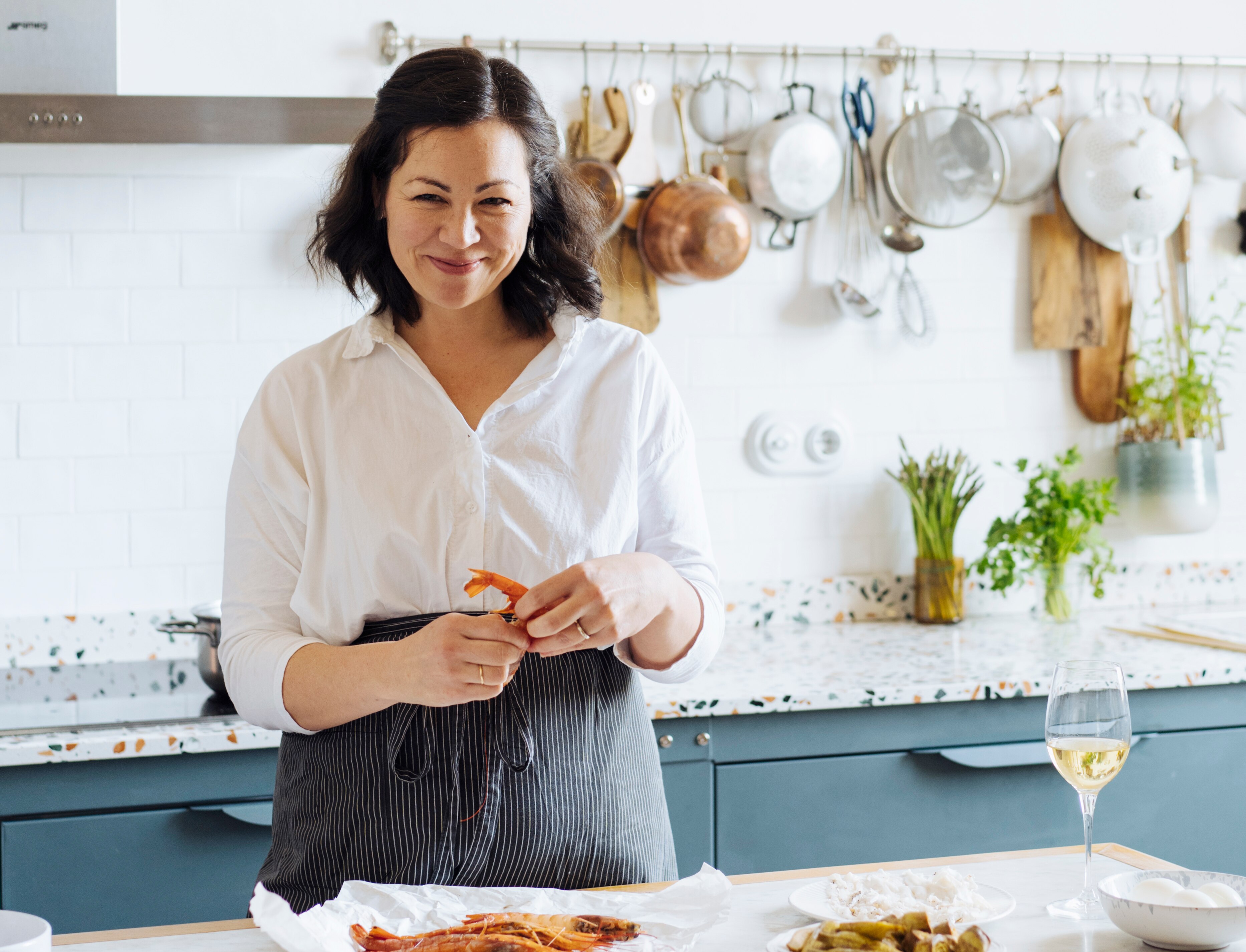 Emiko Davies stands in her kitchen holding a prawn and smiling at the camera