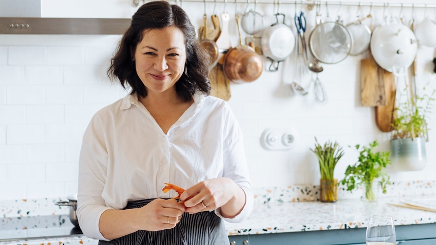 Emiko Davies stands in her kitchen holding a prawn and smiling at the camera