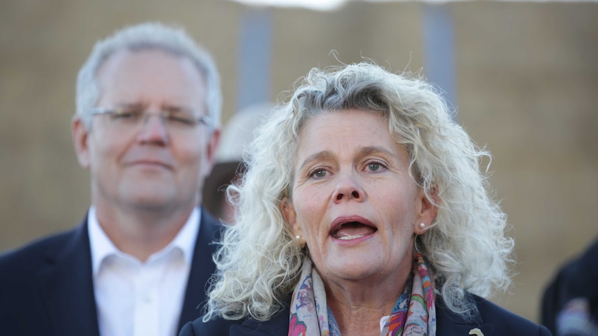 A woman speaks at a press conference with Prime Minster Scott Morrison watching on over her shoulder