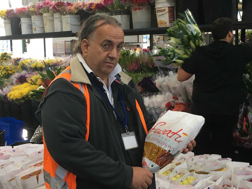 A man in an orange vest holds a bouquet of flowers at a market.