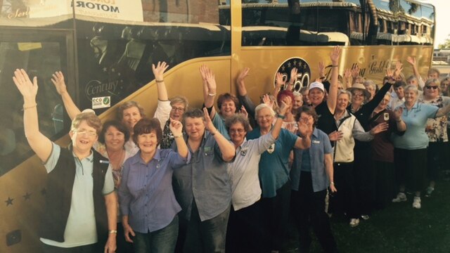 Women waving in front of a gold bus.