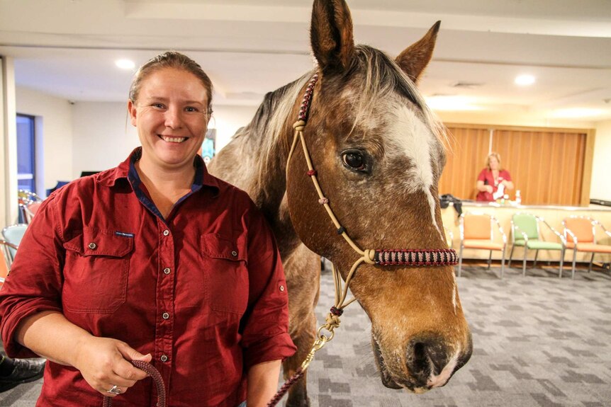 A woman stands holding the reins of a horse inside a retirement home.