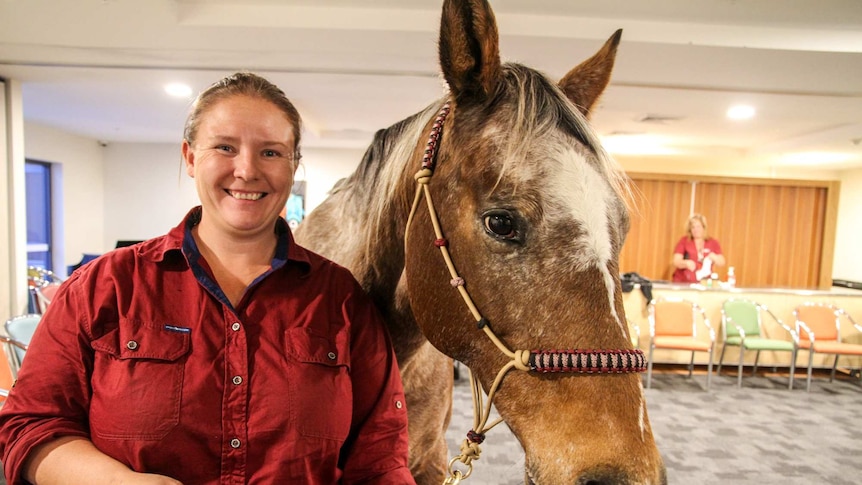 A woman stands holding the reins of a horse inside a retirement home.
