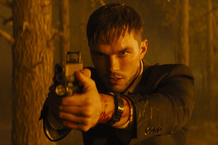 Film still of Nicholas Hoult as Patrick holding a gun in front of a forest fire in Those Who Wish Me Dead