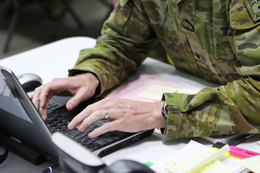 Close up shot of man in camo uniform using a computer.