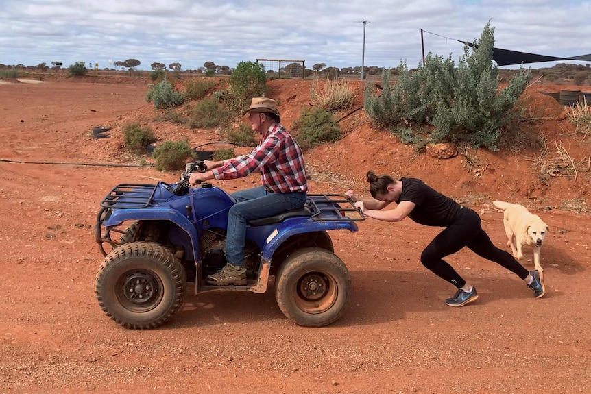 A young woman pushing a man on a quad bike