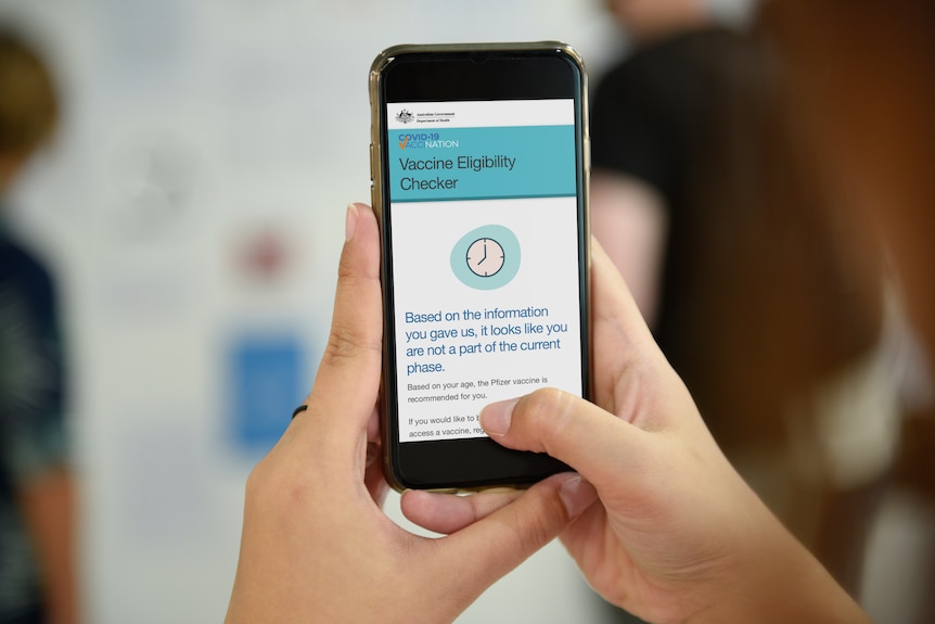 A woman holds a phone displaying a website that says she is not eligible for a COVID-19 vaccine.