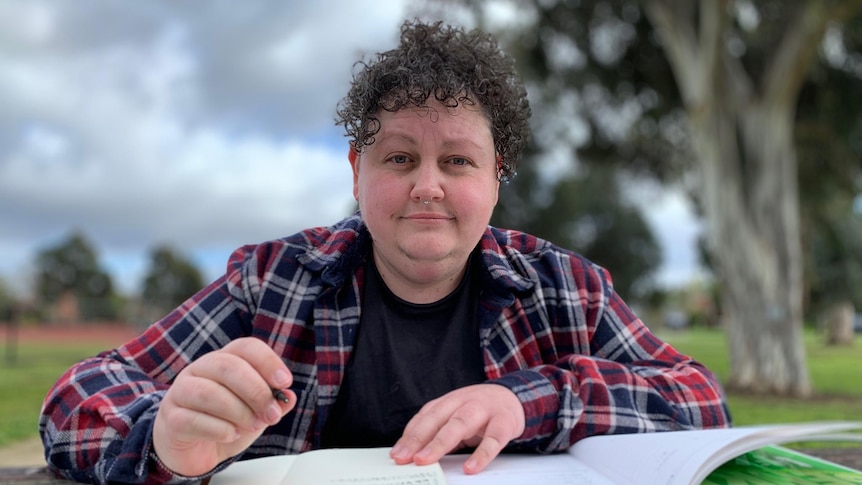 Teddy White holds a pen above a notebook while sitting in a park.