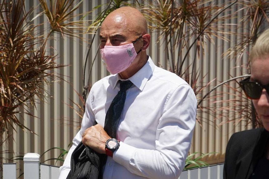 NT Chief Health Officer Hugh Heggie leaves Darwin Local Court. He is wearing a pink face mask and a shirt and tie.